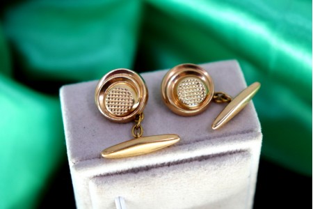 Botões de punho em ouro de formato botão relevado e guilhochado no centro.